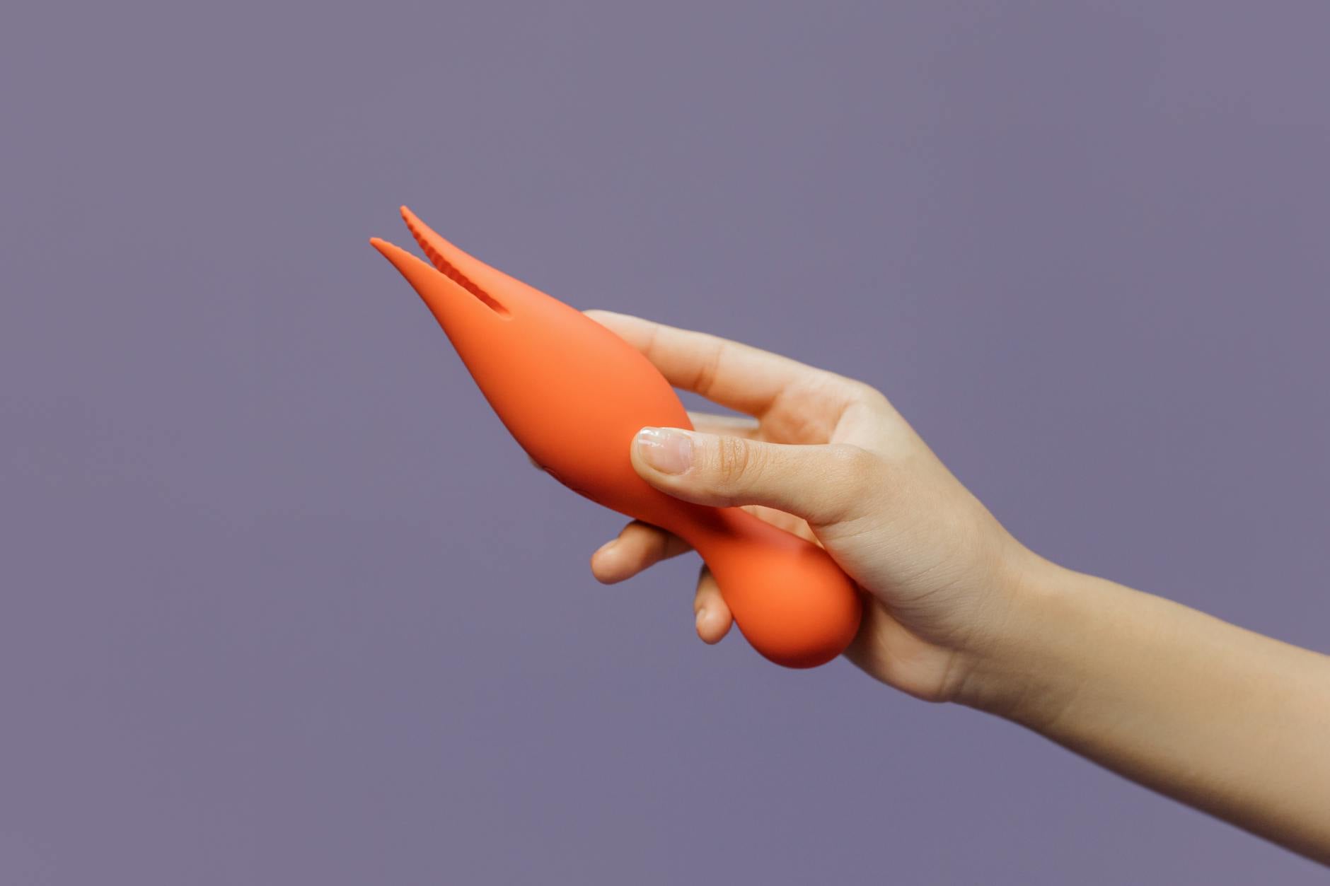 Hand holding a lemon-colored vibrator against a minimalist purple backdrop, showcasing modern clitoral pleasure design