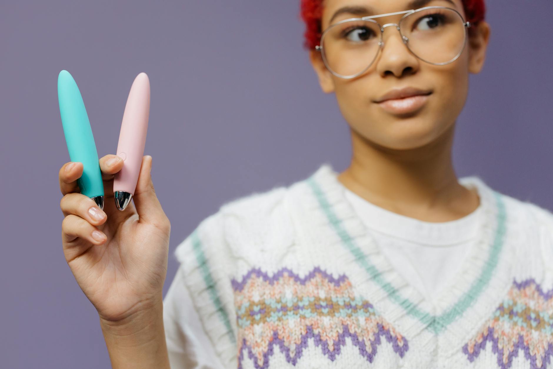 Hands holding colorful vibrators against a purple background, representing sexual wellness and self-exploration