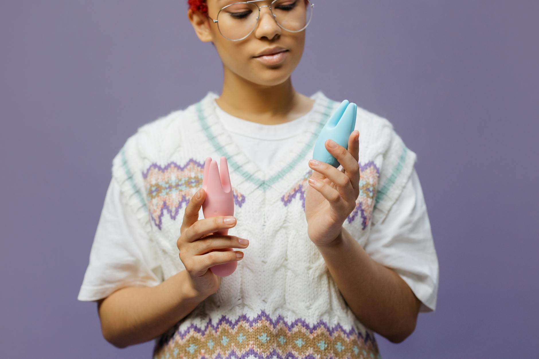 Woman holding blue and pink silicone vibrators thoughtfully, exploring sensation with intention.