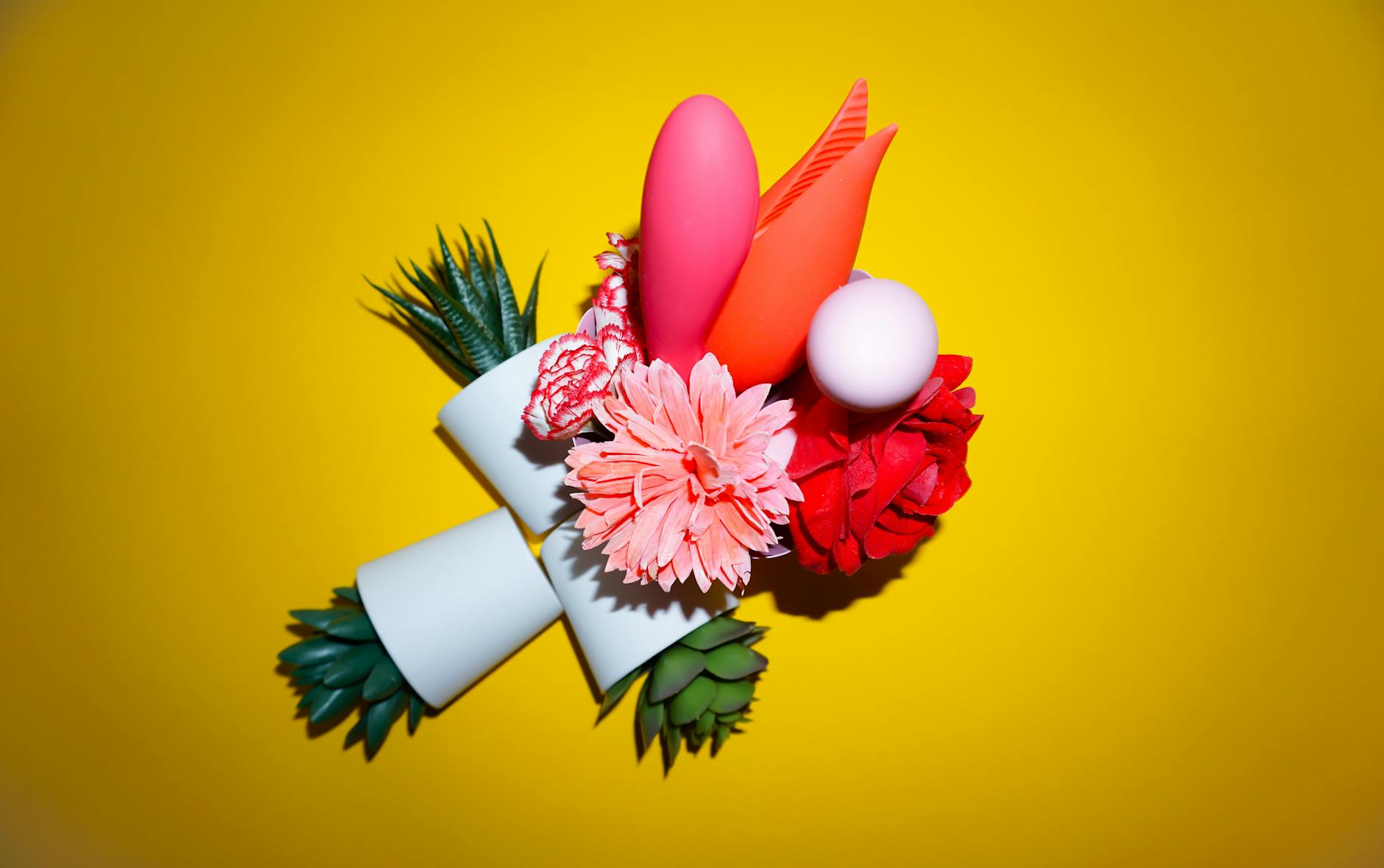 Vibrant arrangement of colorful clitoral vibrators with flowers on a bright yellow background.