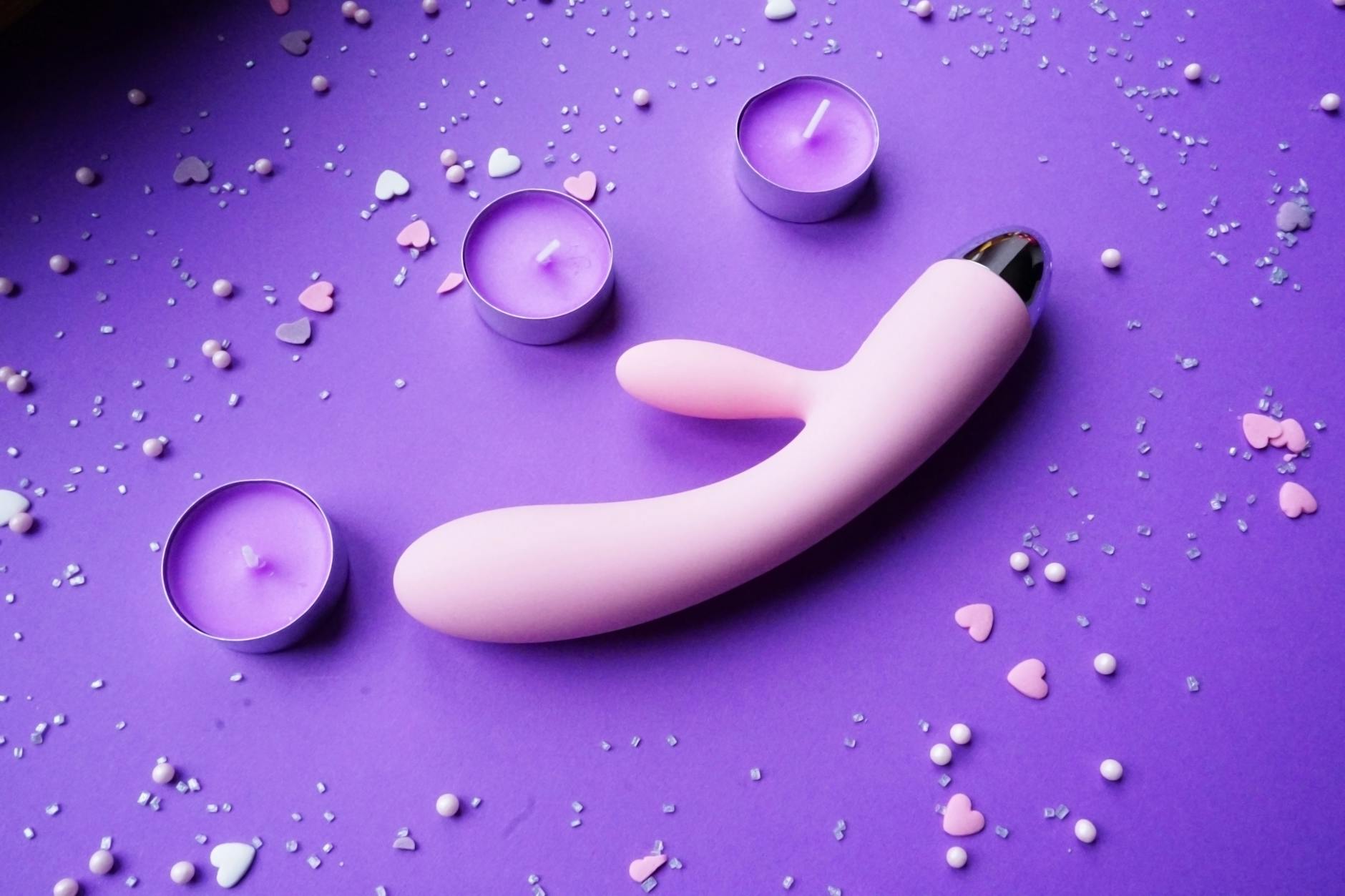 A pink vibrator displayed on a purple surface with candles and heart confetti, symbolizing self-care and reclaimed pleasure after divorce.